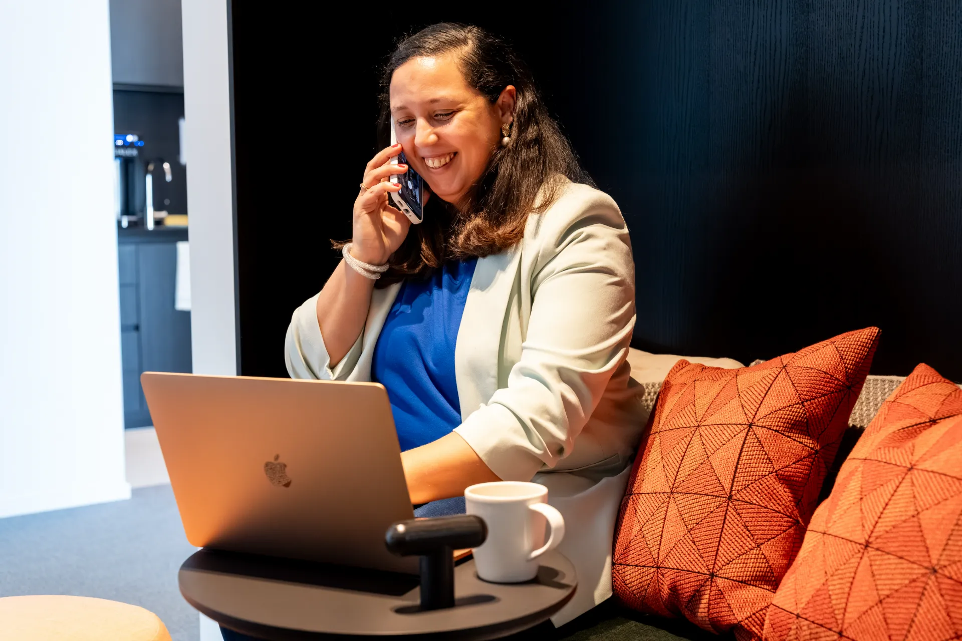 Financieel advies: helderheid en rust voor KMO's. Lachende financieel adviseur Samra Daoud belt en werkt op laptop in een moderne kantooromgeving.