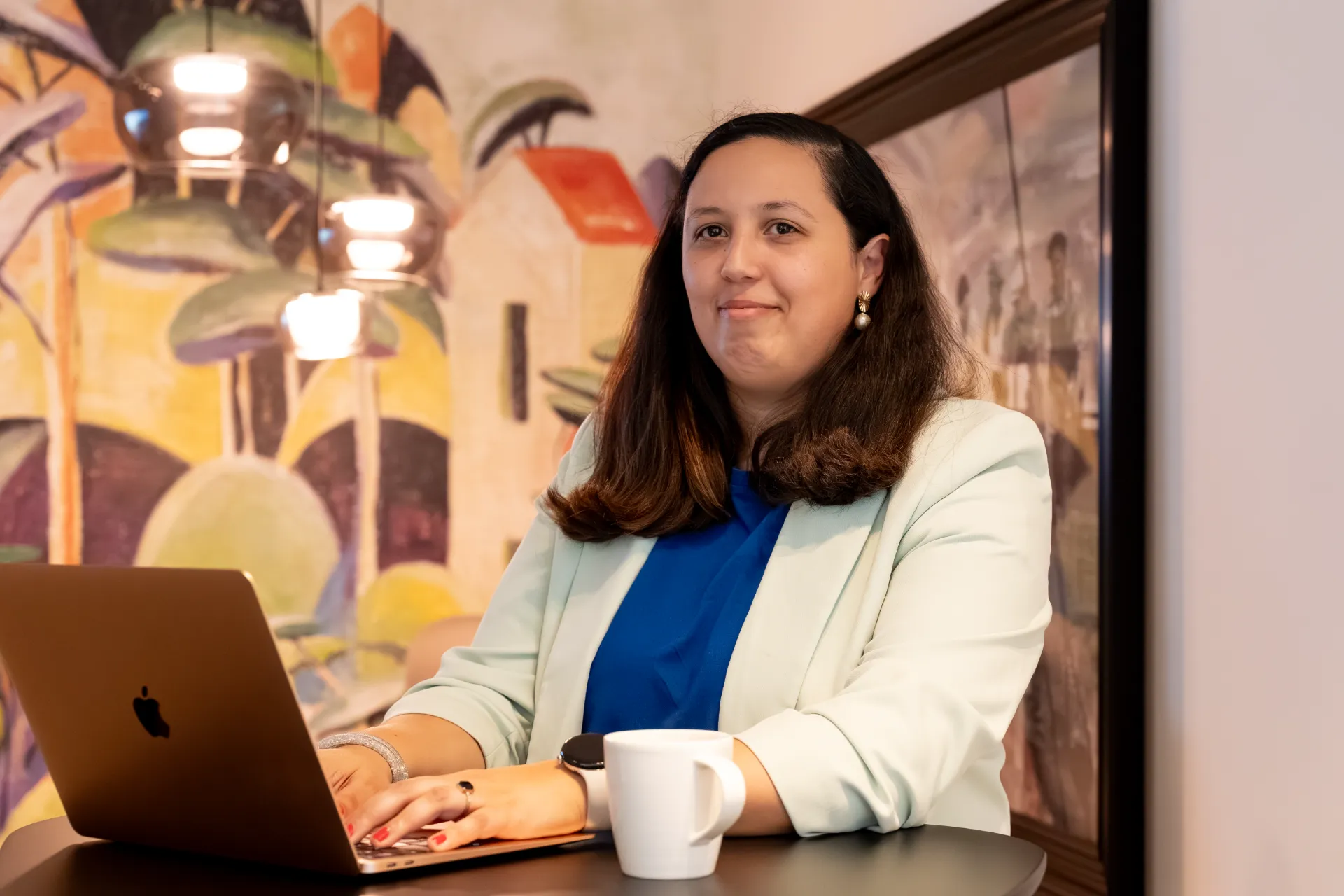 Financieel advies KMO: Cijfers helder, toekomst zeker. Samra Daoud, financieel adviseur, zit glimlachend aan een tafel met een laptop in een modern kantoor.